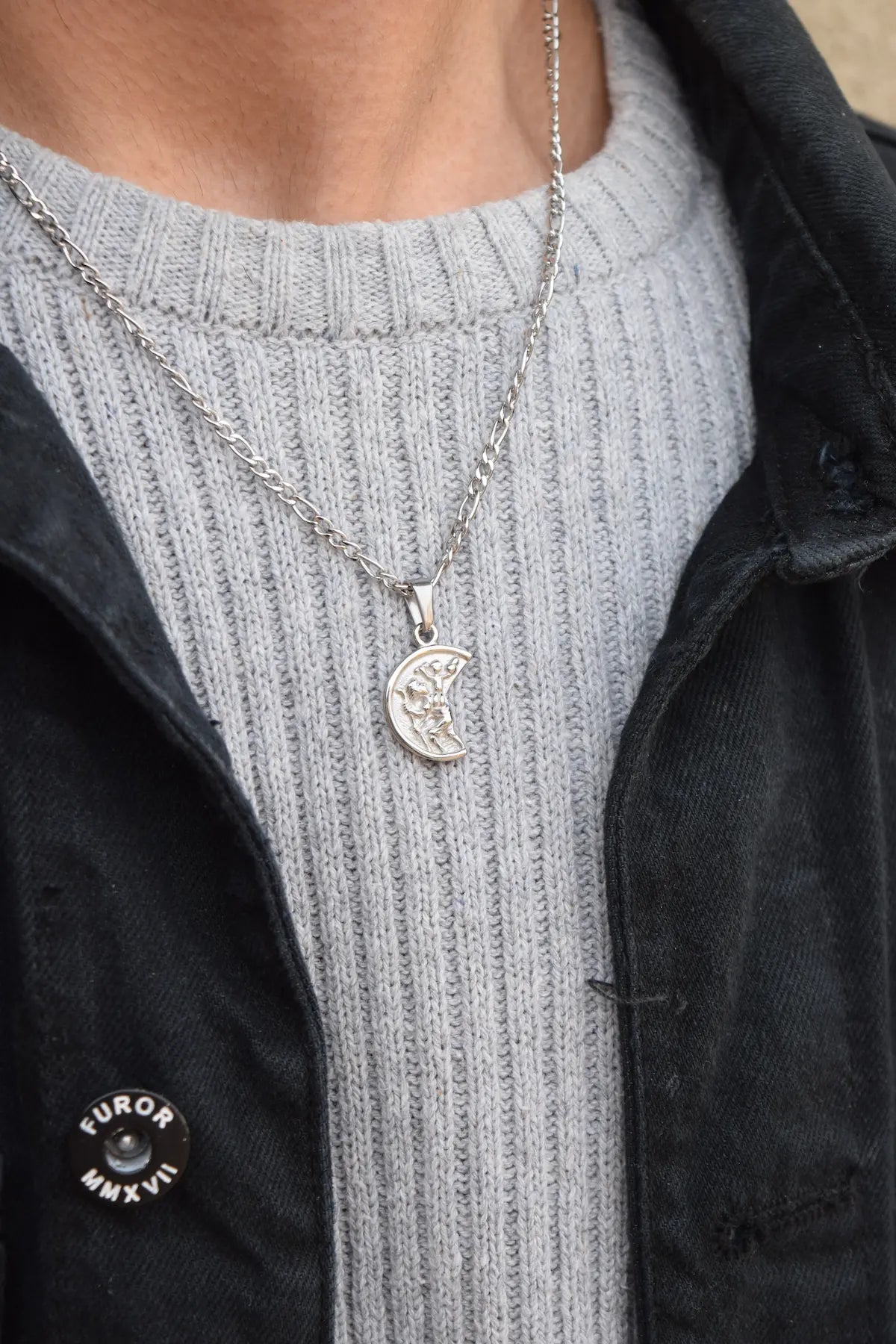 A close-up of the Christopher pendant being worn around the neck. The pendant has a detailed design, hanging on a sleek chain, styled to highlight its shine and craftsmanship.