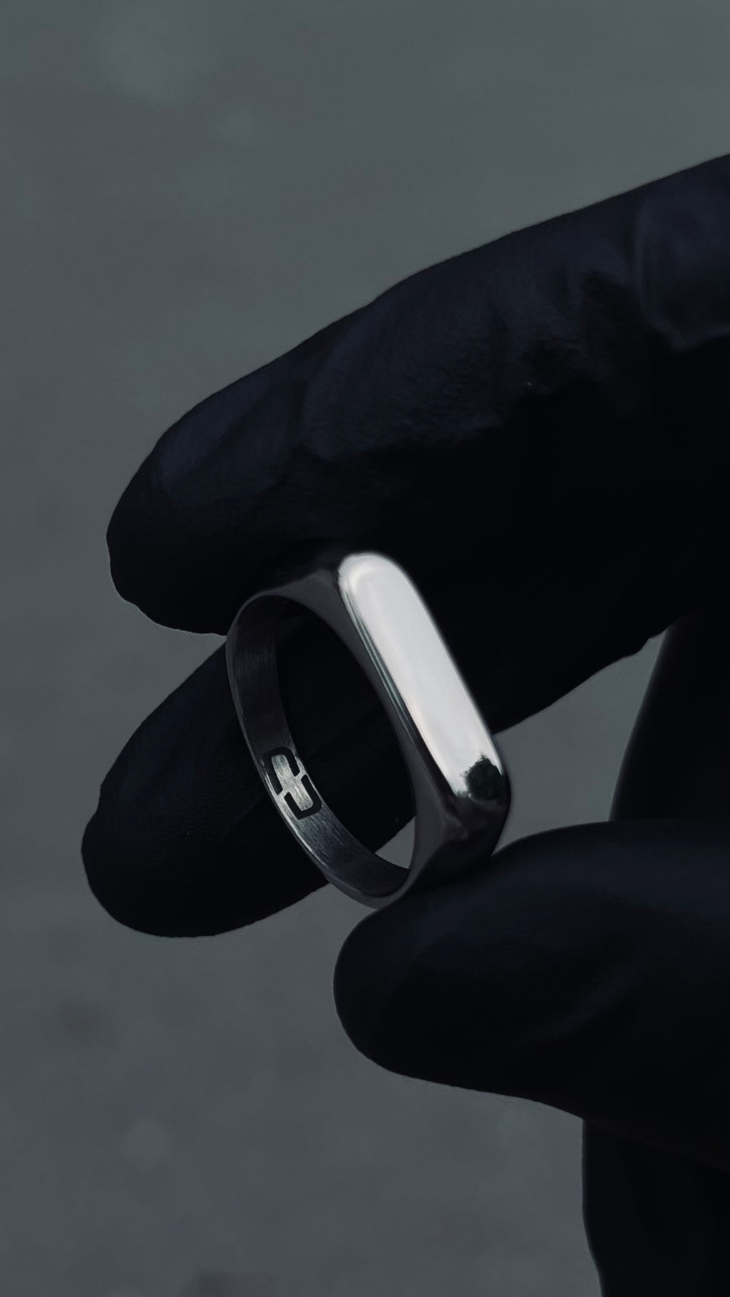A stainless steel signet ring held between fingers, with a plain and slightly domed design.