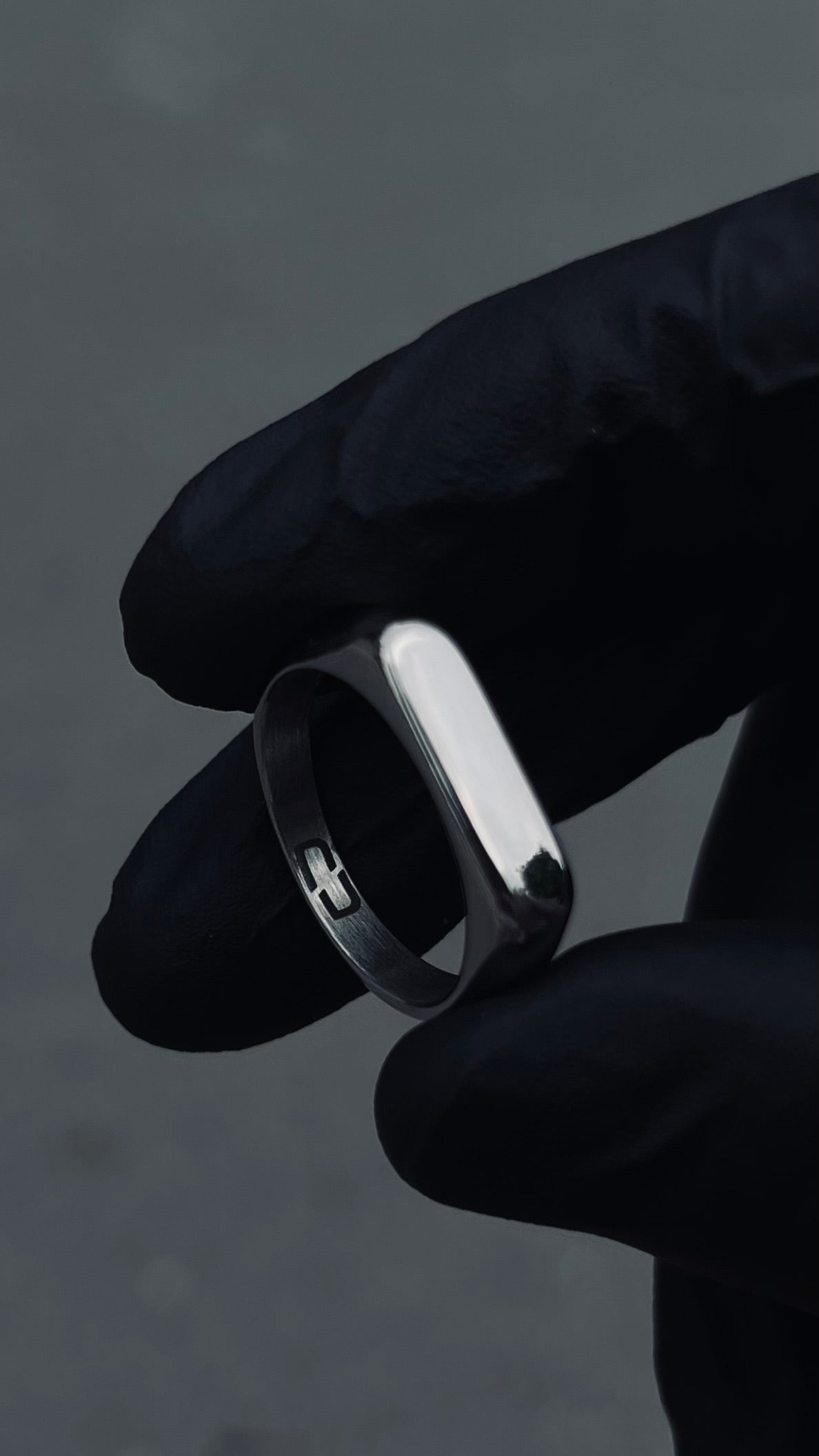 A stainless steel signet ring held between fingers, with a plain and slightly domed design.